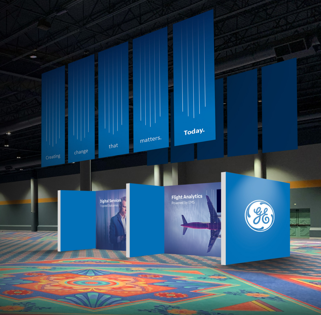 Environmental Branding Design - A large lobby area where an environmental branding experience for GE is shown. Posters hanging from the ceiling read "Creating change that matters today" and there are images of people and an airplane on large standing booth graphics on the floor.