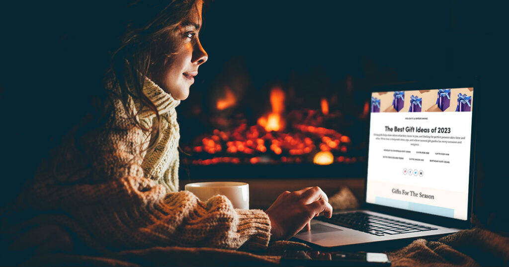a woman looks at her laptop while sitting in front of a fire