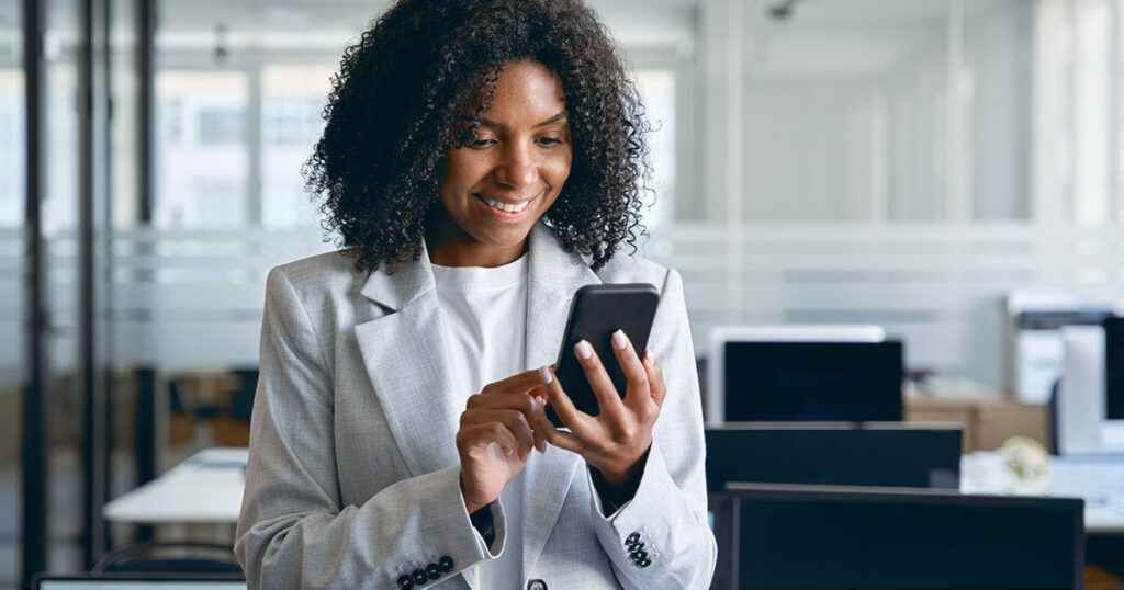 how to get the reader's attention - a woman with curly hair and wearing a grey suit looking happily at her smart phone